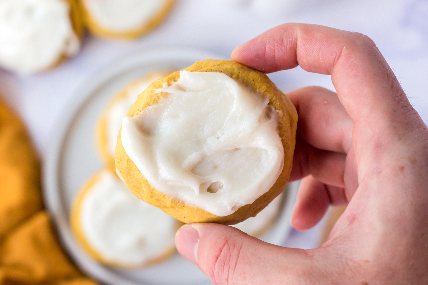 hand holding a pumpkin cookie with frosting