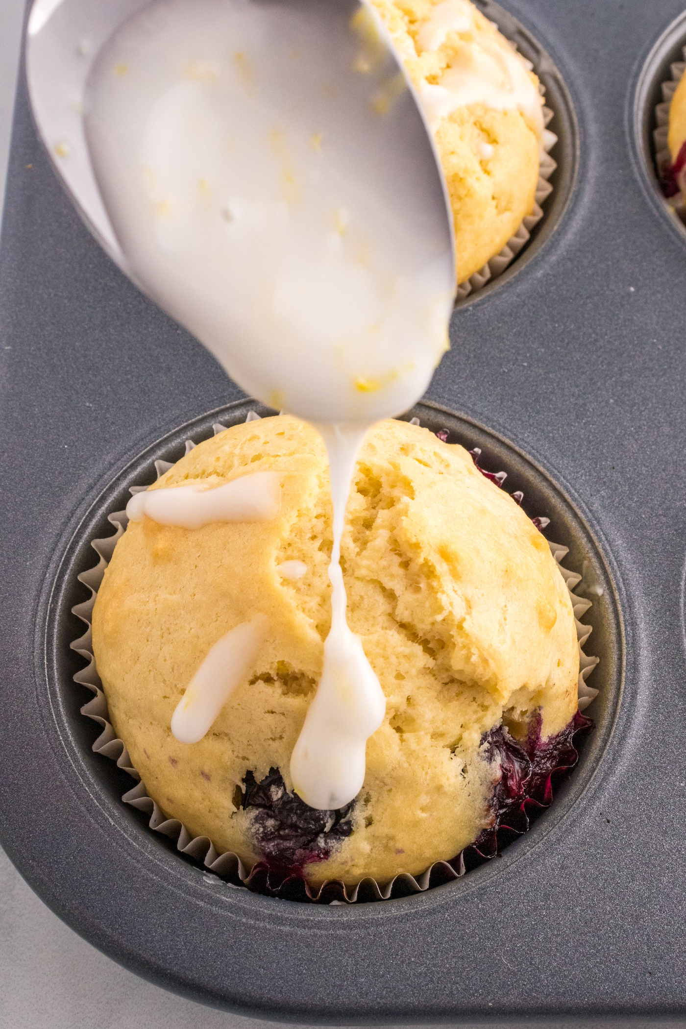 Drizzling the lemon glaze onto a muffin