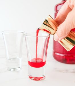pouring grenadine into a shot glass
