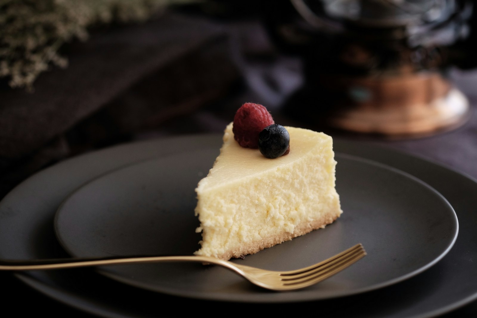 Slice of creamy cheesecake with a berry on a dark plate