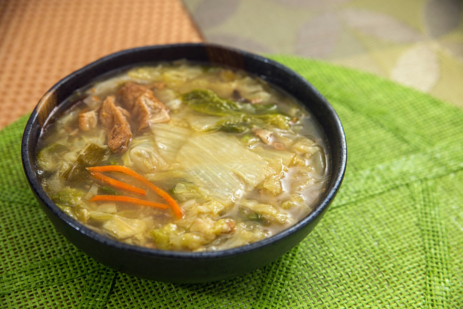 Bowl of chicken noodle soup with vegetables on a green table