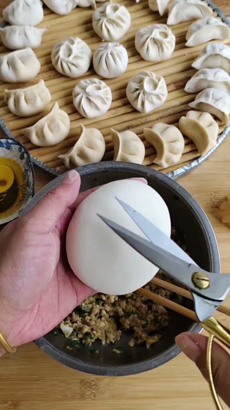 Hands folding dumplings with scissors and a bowl of filling