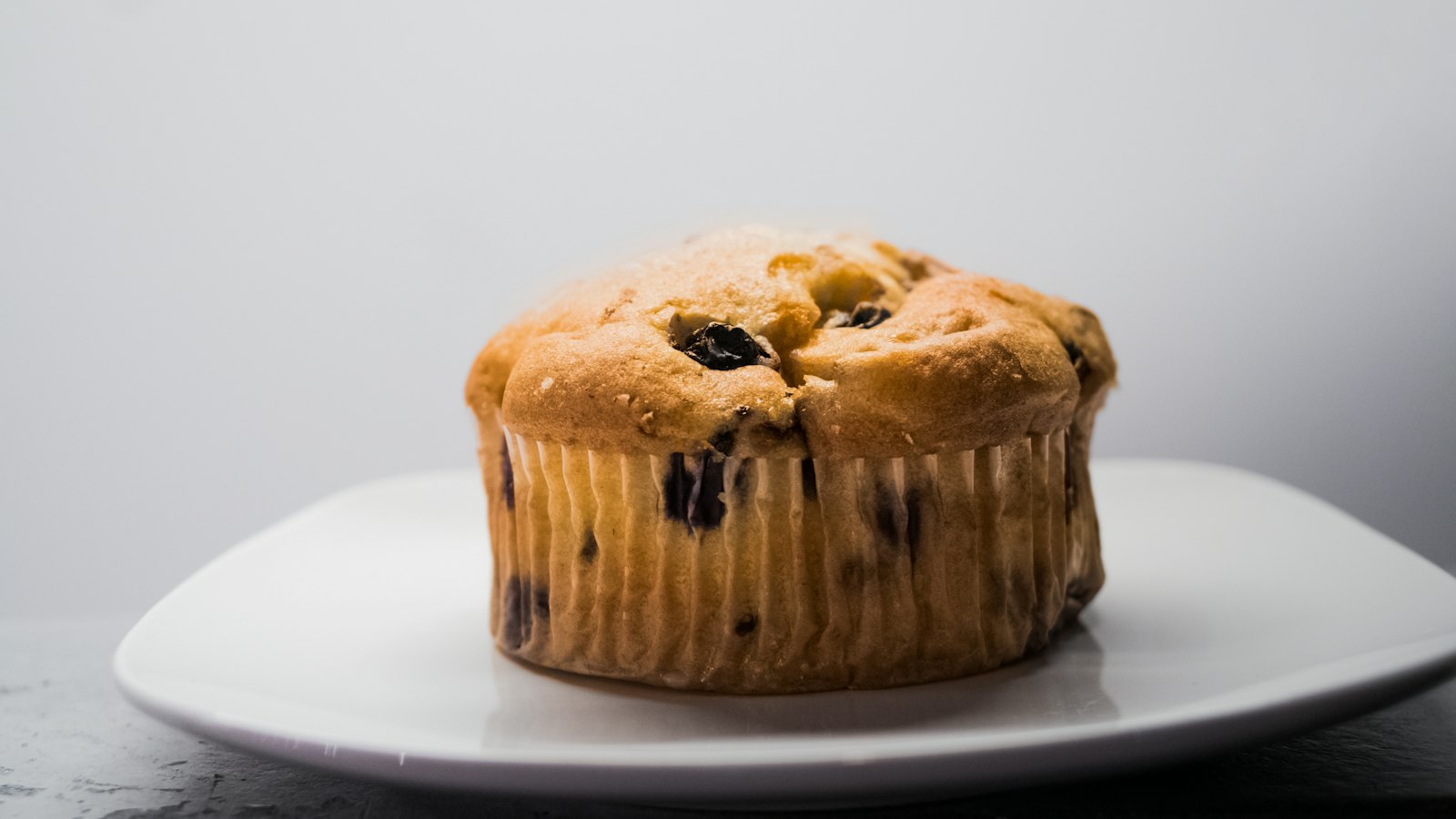 Golden muffin studded with red berries on a white plate