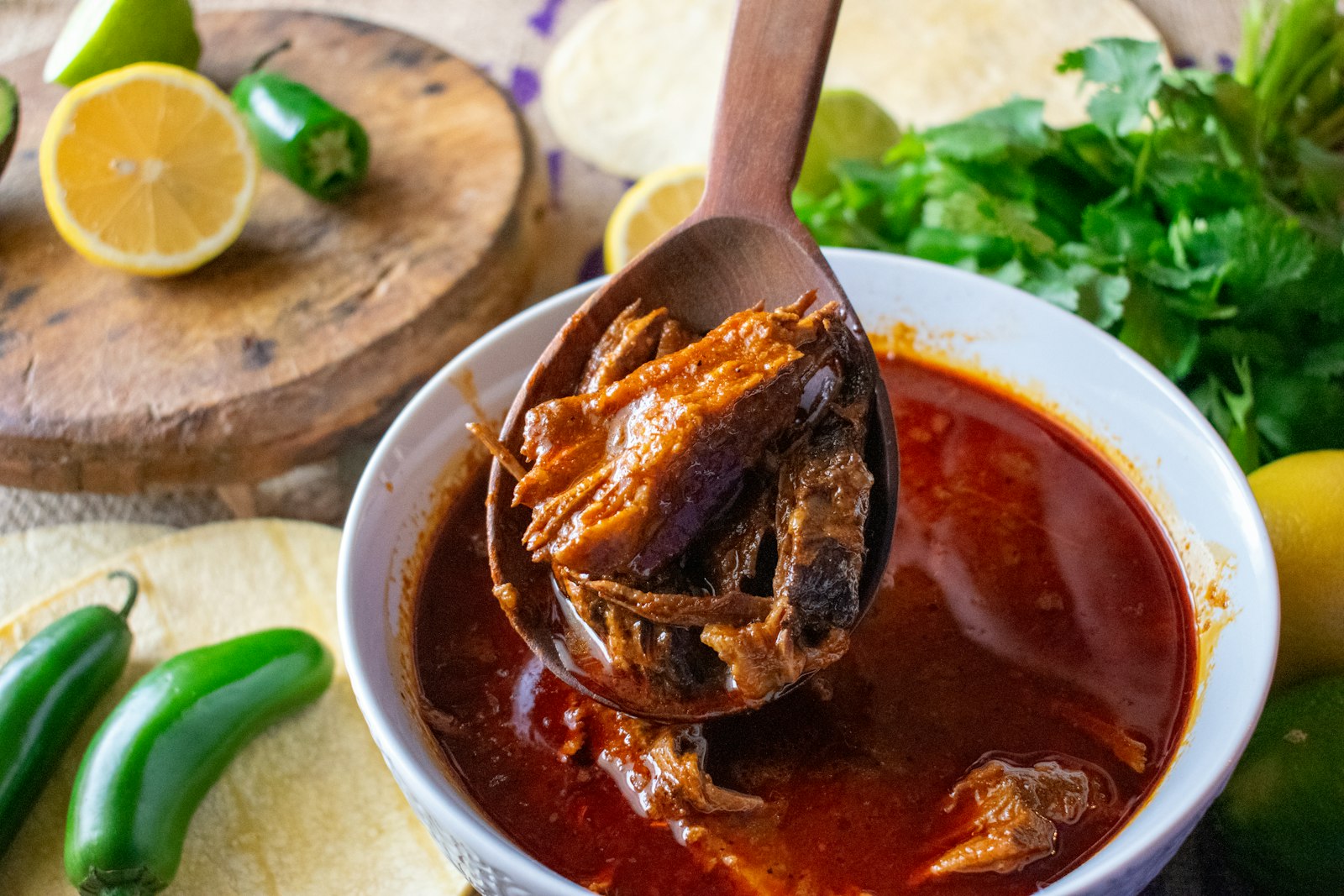 Ladle of shredded beef birria in rich red consomme