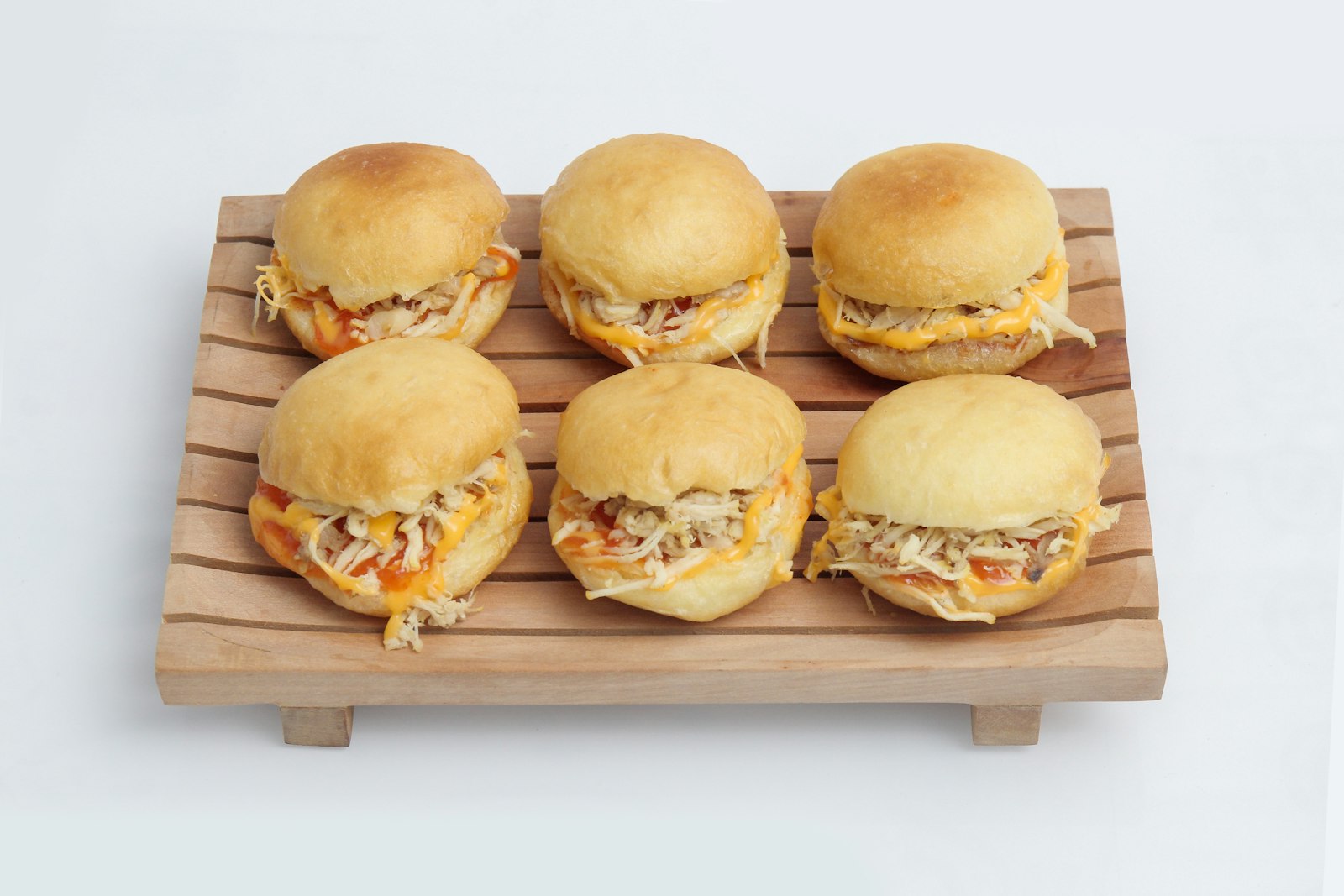 Pulled BBQ chicken sliders lined up on a wooden board
