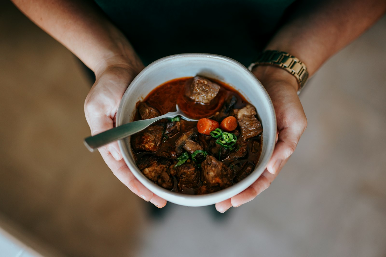 Hands holding a bowl of slow cooked beef and bean stew