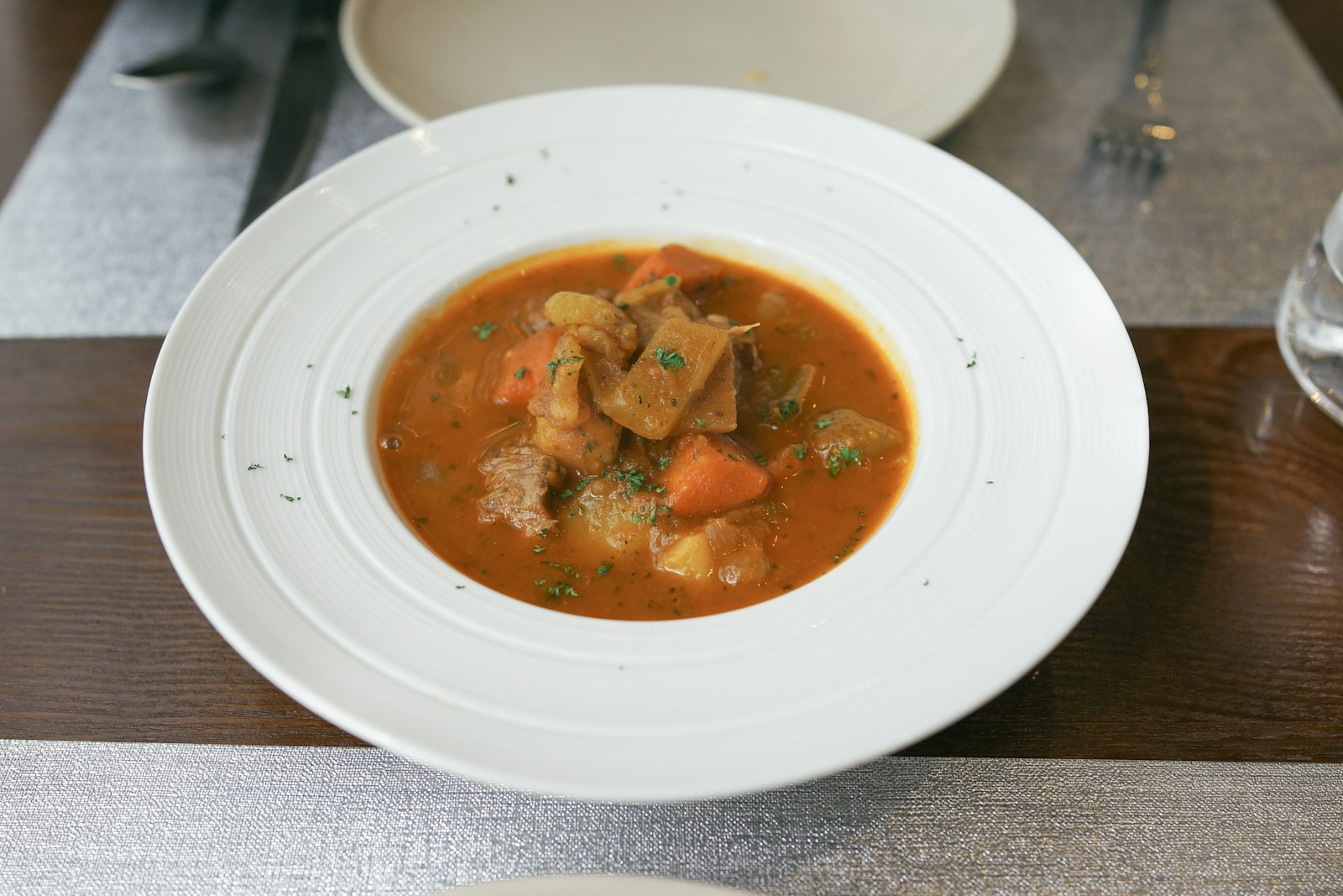 Hearty beef and barley soup with vegetables in a white bowl