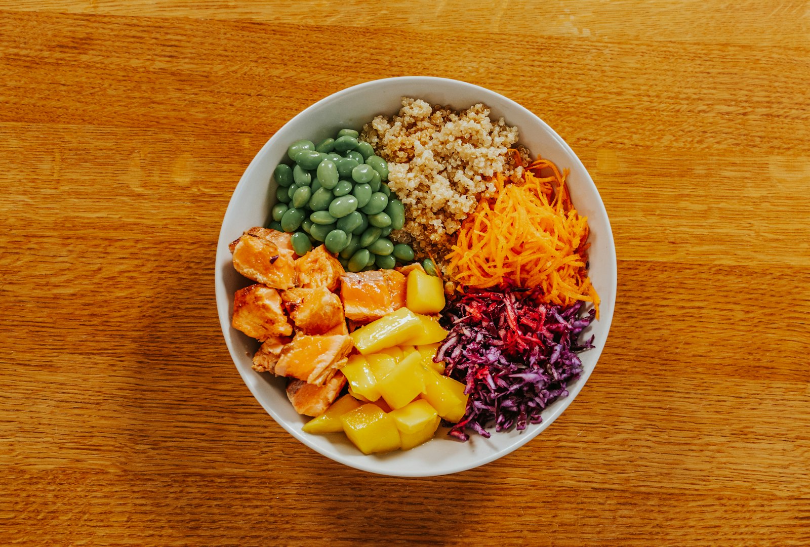 Edamame, mango, carrot and red cabbage buddha bowls on a wooden table