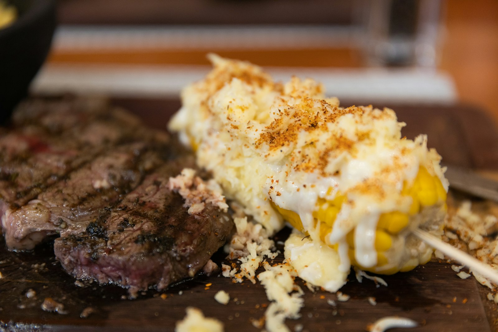 Elote with cheese and chili next to grilled steak