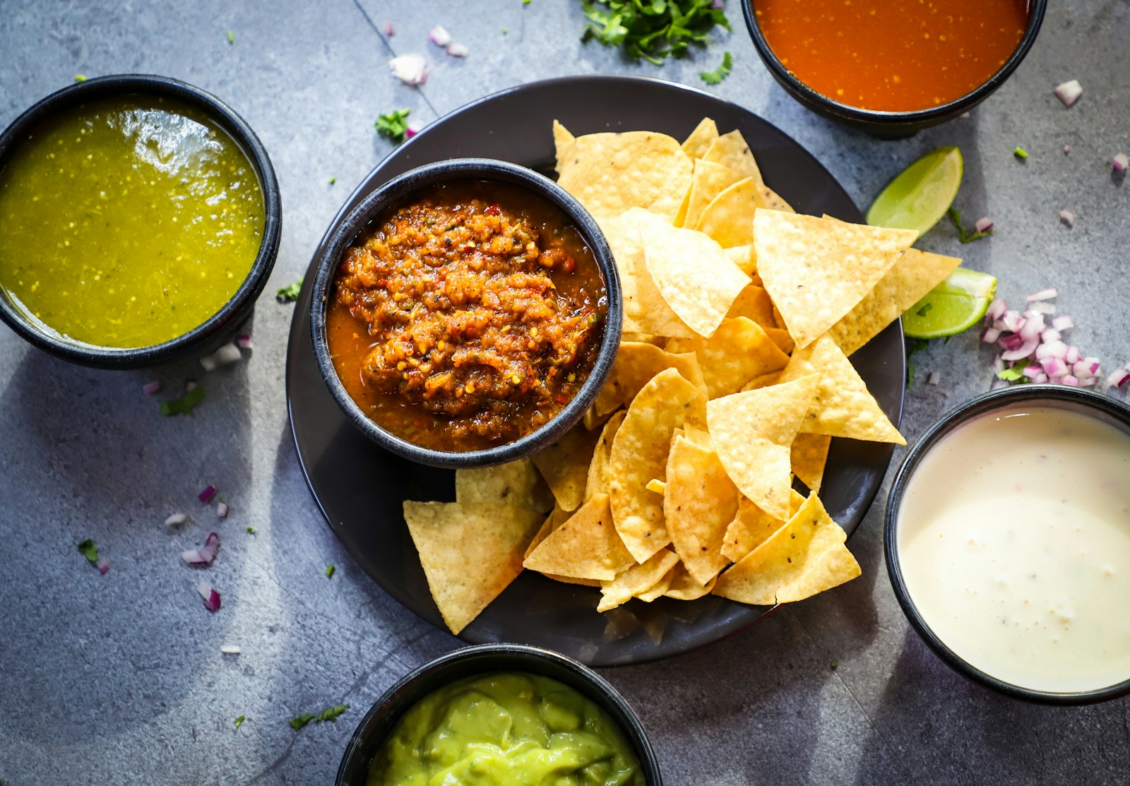 Salsa, guacamole and chips on a dark table