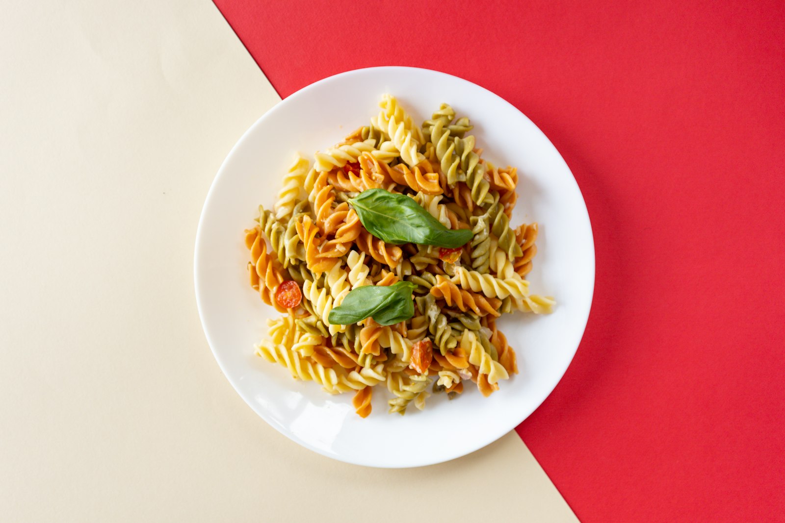 Tricolor fusilli pasta salads with fresh basil on a white plate