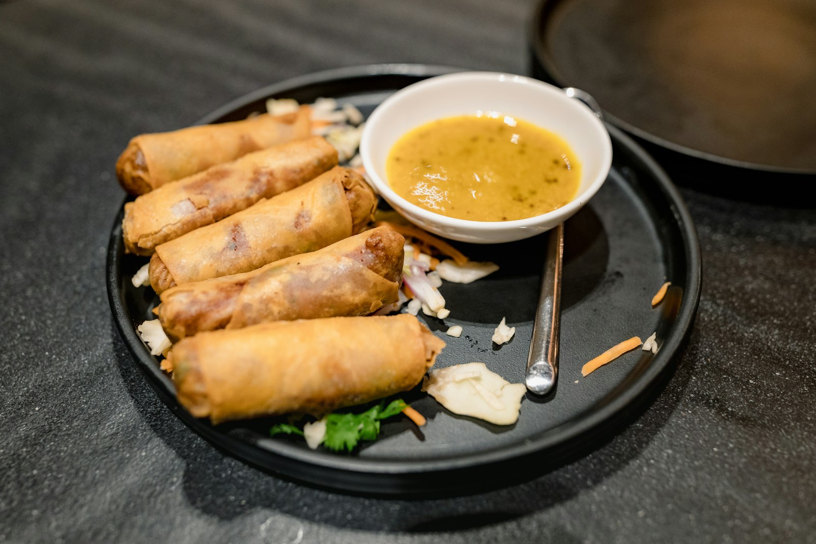 Golden baked spring rolls with dipping sauce on a black plate