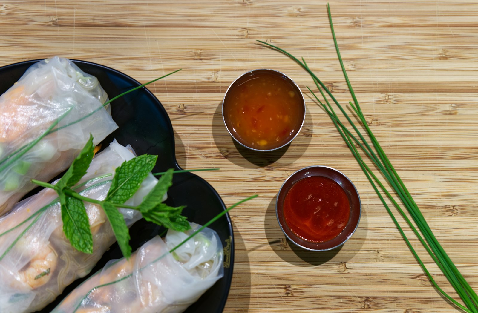 Rice paper wraps with mint and two dipping sauces on a bamboo board