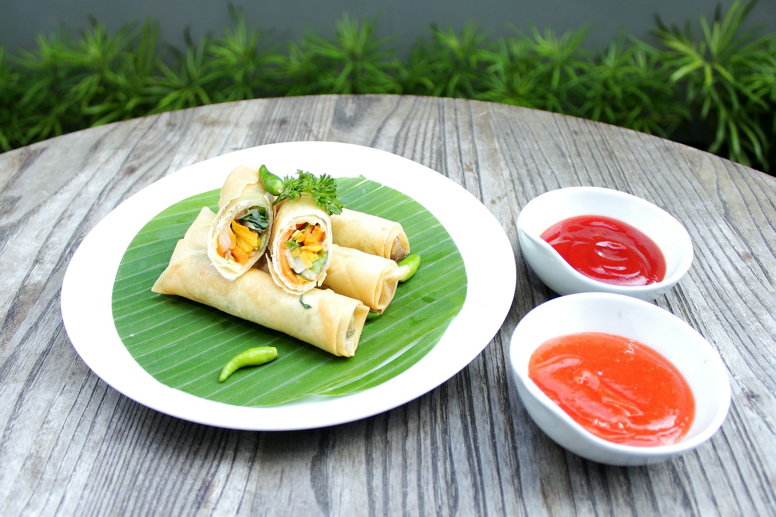 Egg wrapped vegetable rolls on a banana leaf with chili sauces
