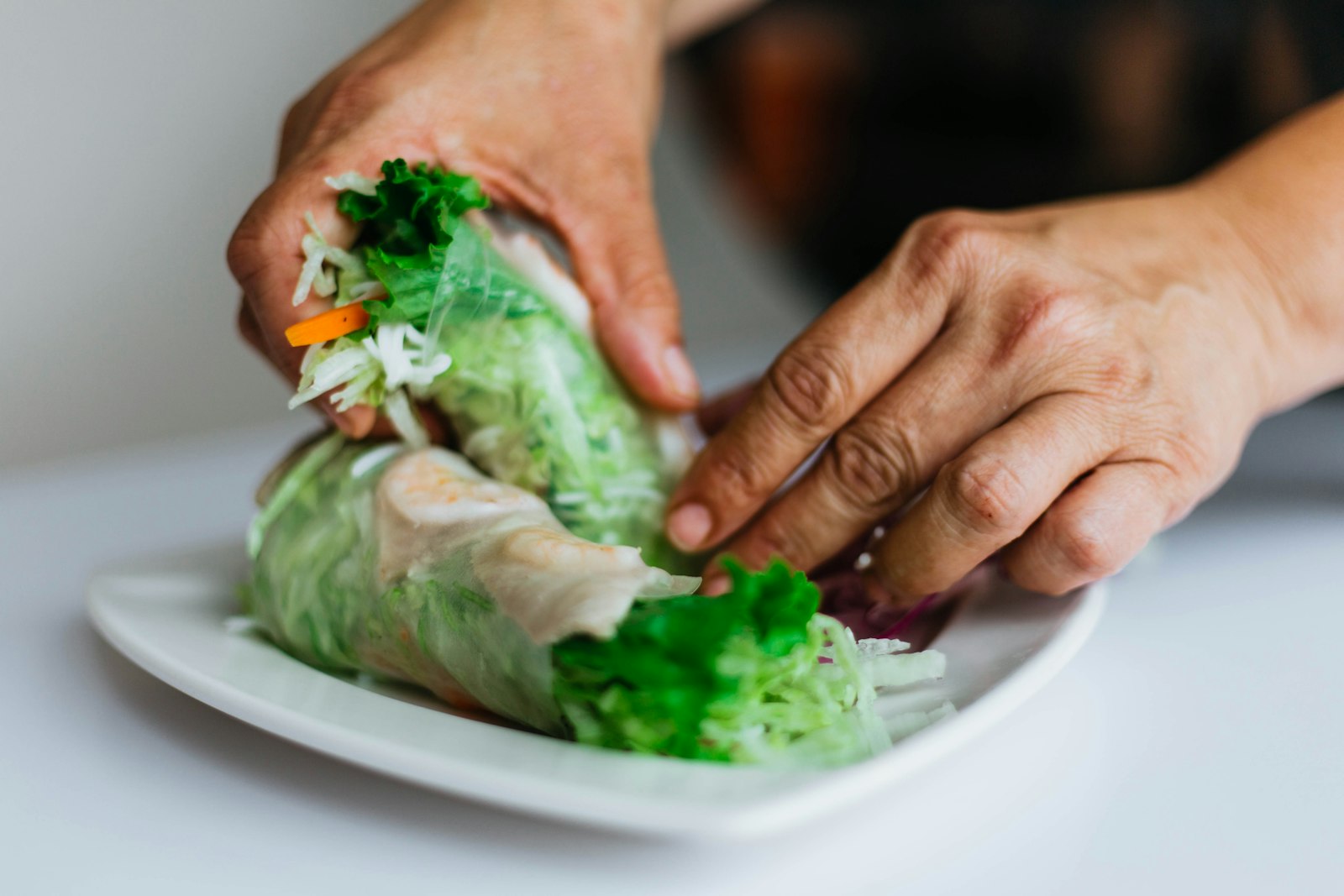 Hands rolling fresh vegetables in rice paper