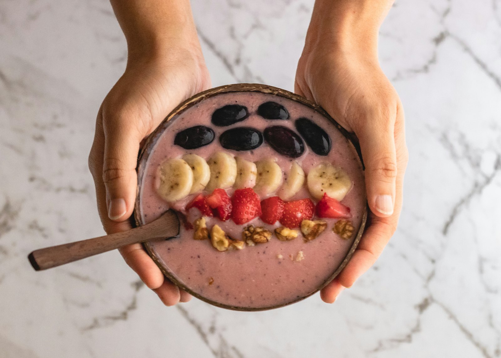 Strawberry banana smoothie bowls held in two hands