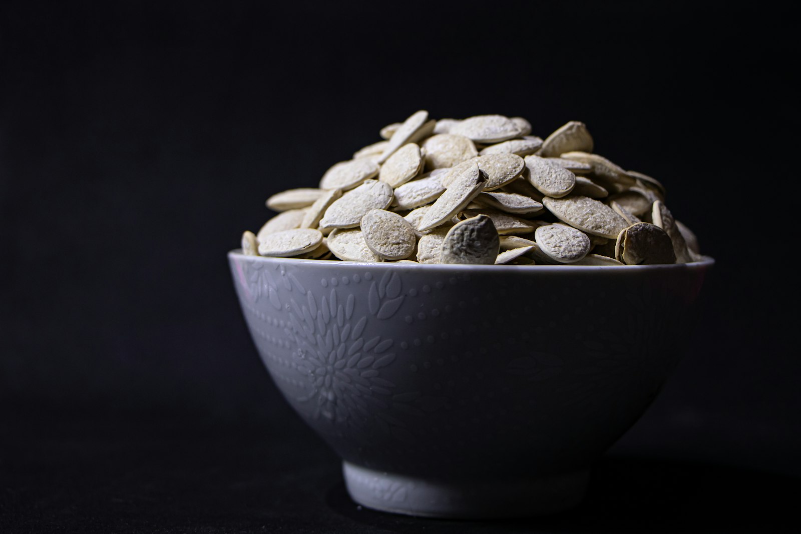 Bowl of pumpkin seeds on a dark table