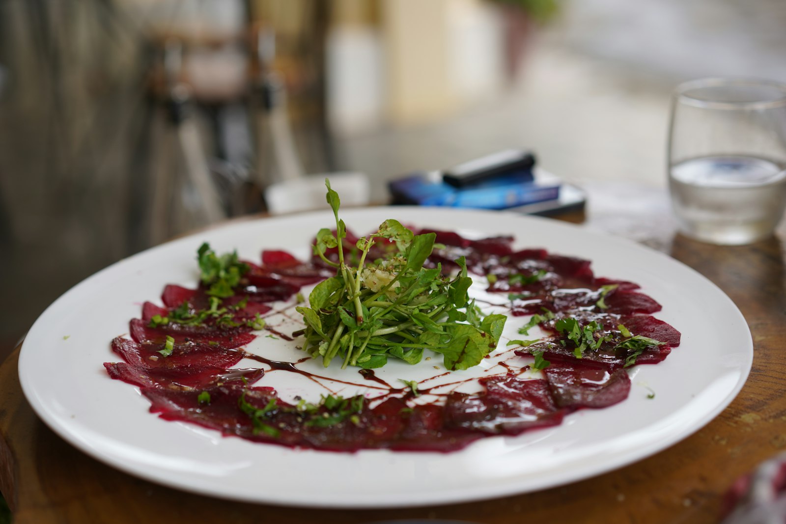 Thin beet carpaccio topped with arugula on a white plate