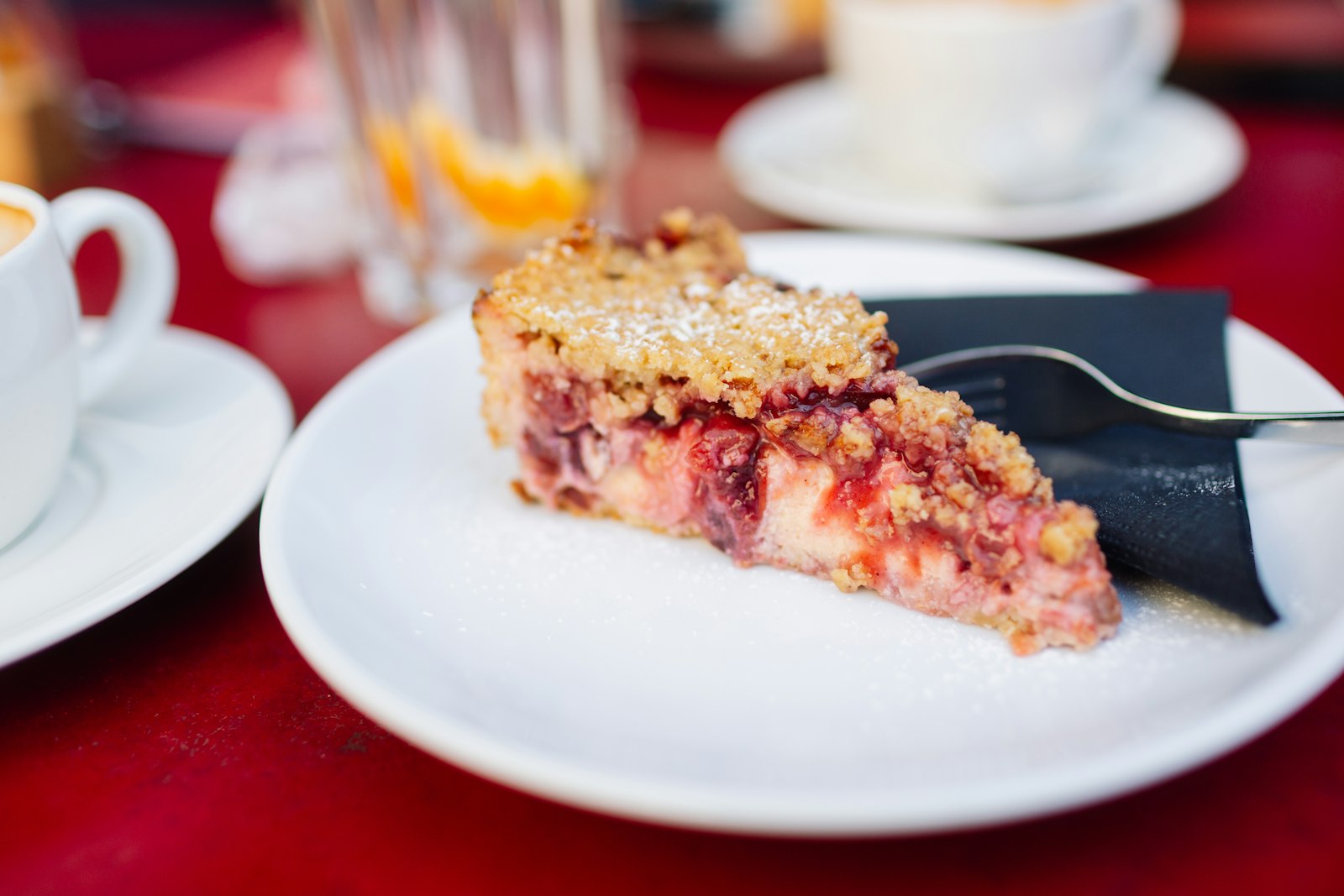 Cherry crumb slice with whipped cream on a red table