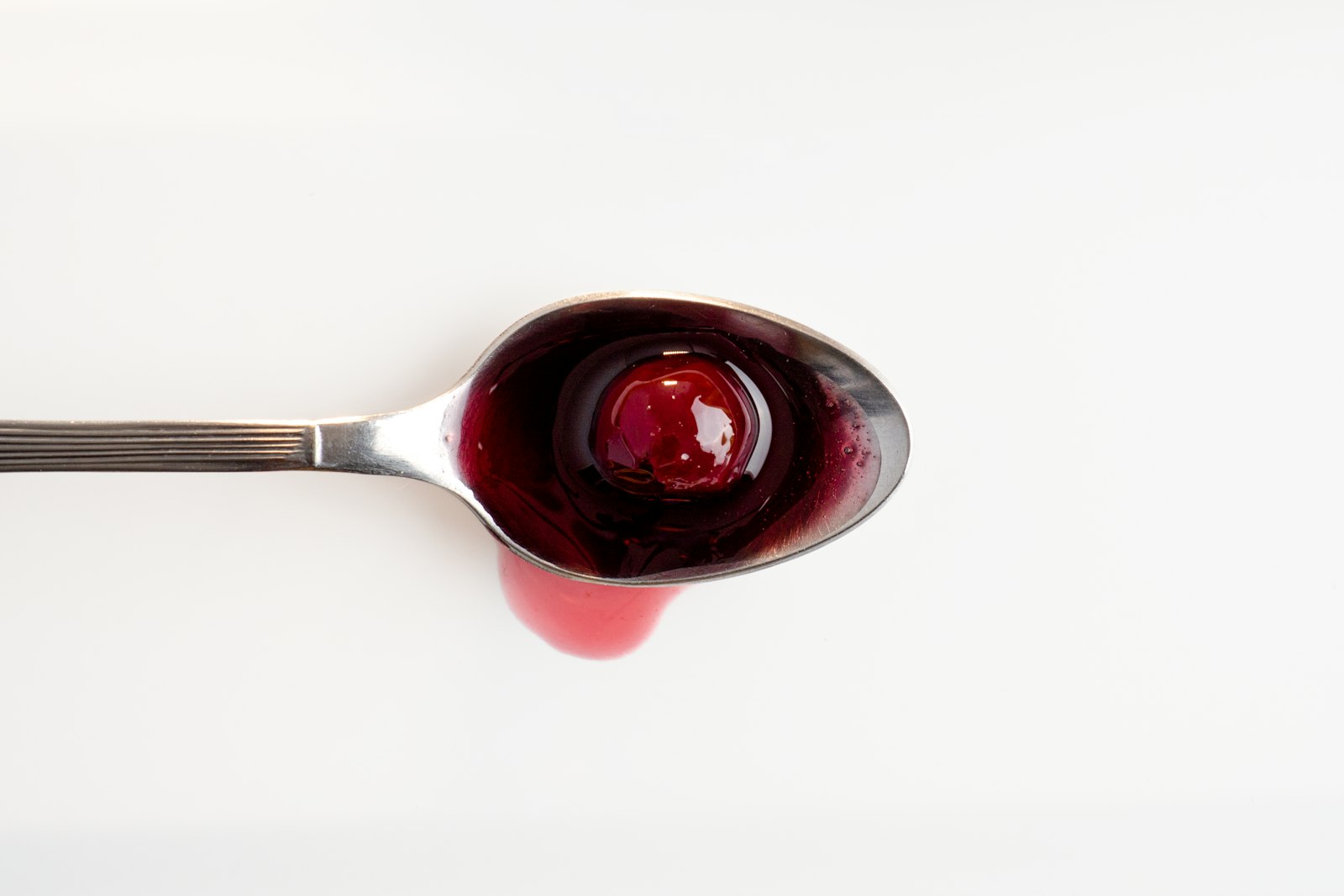 Spoon of dark cherry preserve on a white background