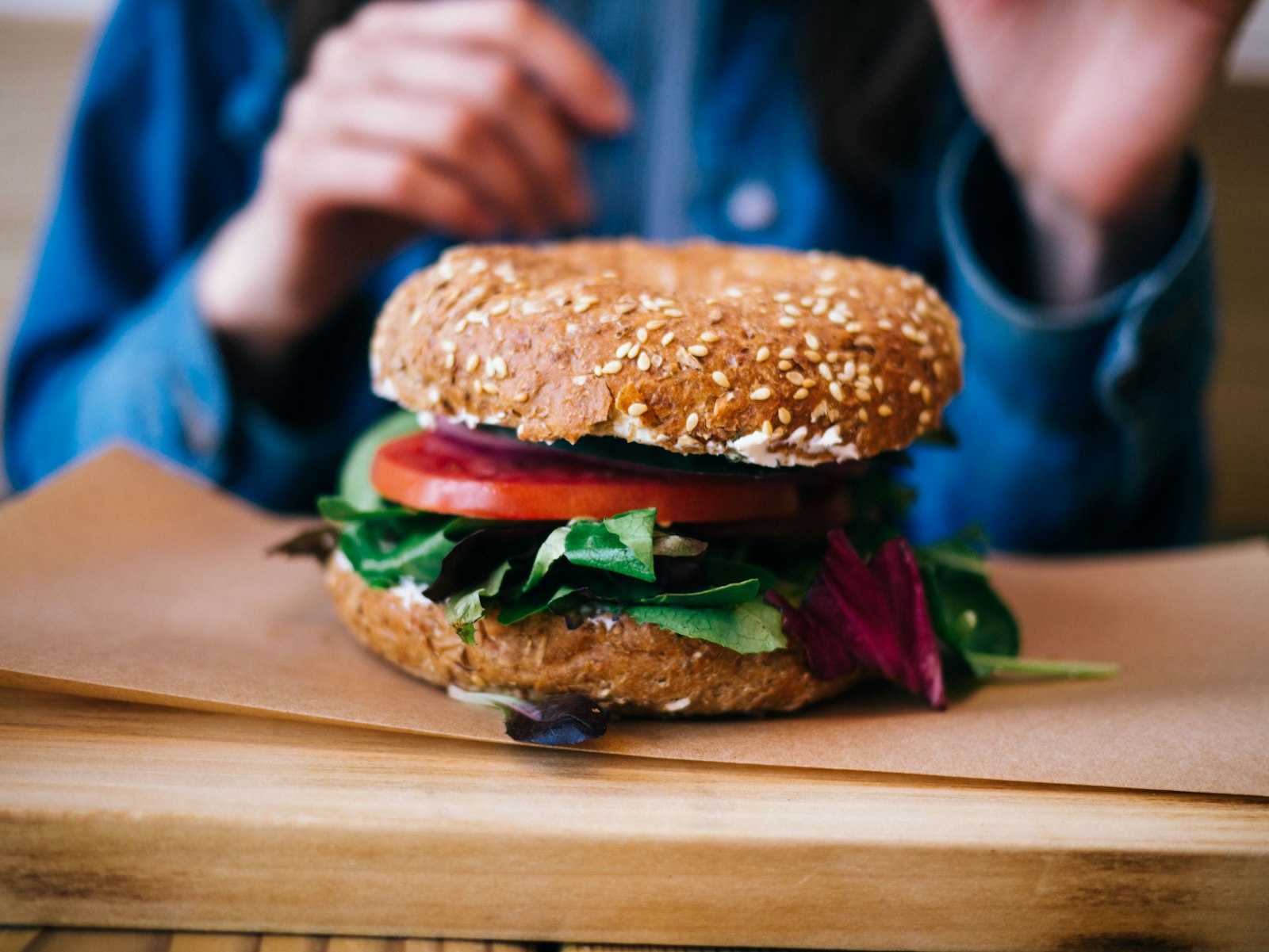 Person holding a seeded bagel stacked with tomato and lettuce