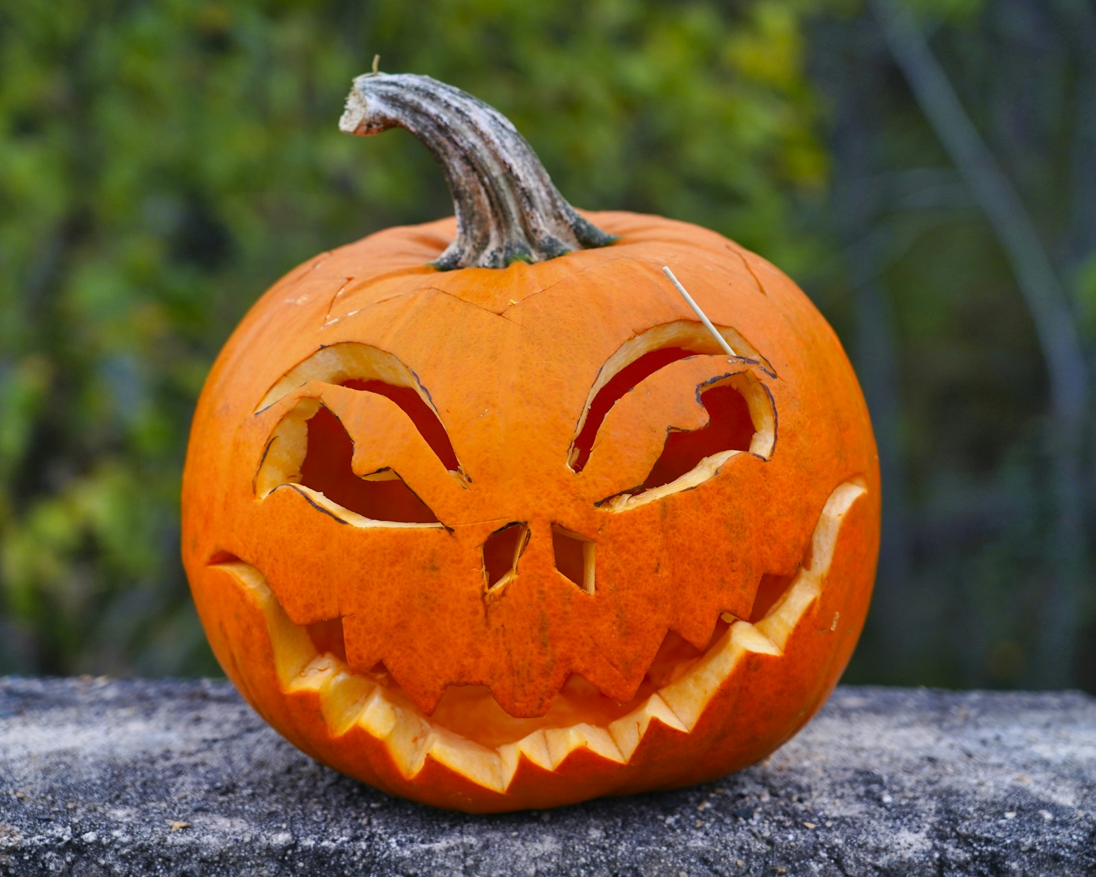 Classic jack o lantern with a wide toothy grin sitting on a stone wall in daylight