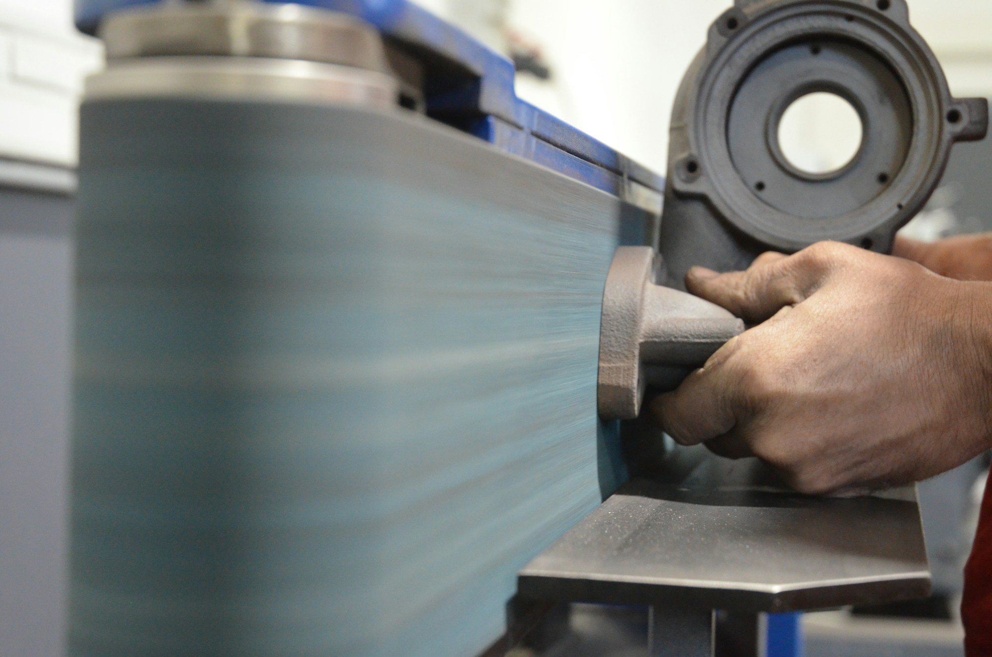 A metal part being smoothed on a workshop belt sanding machine