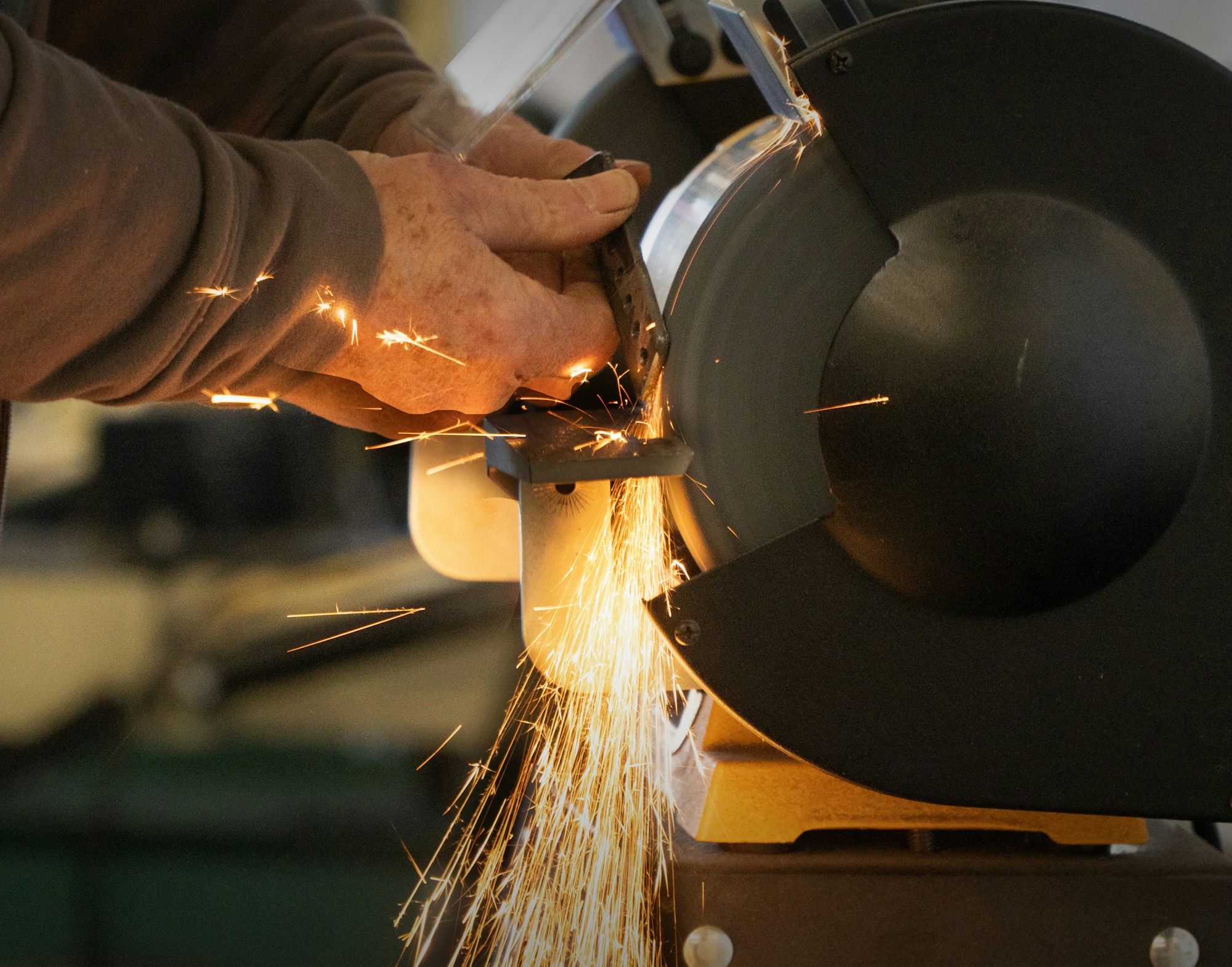 Sparks flying as a metal part is ground on a bench grinder in a workshop