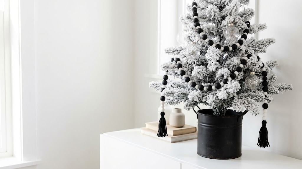 Small flocked tabletop tree in a black pot draped with a black and white wood bead garland