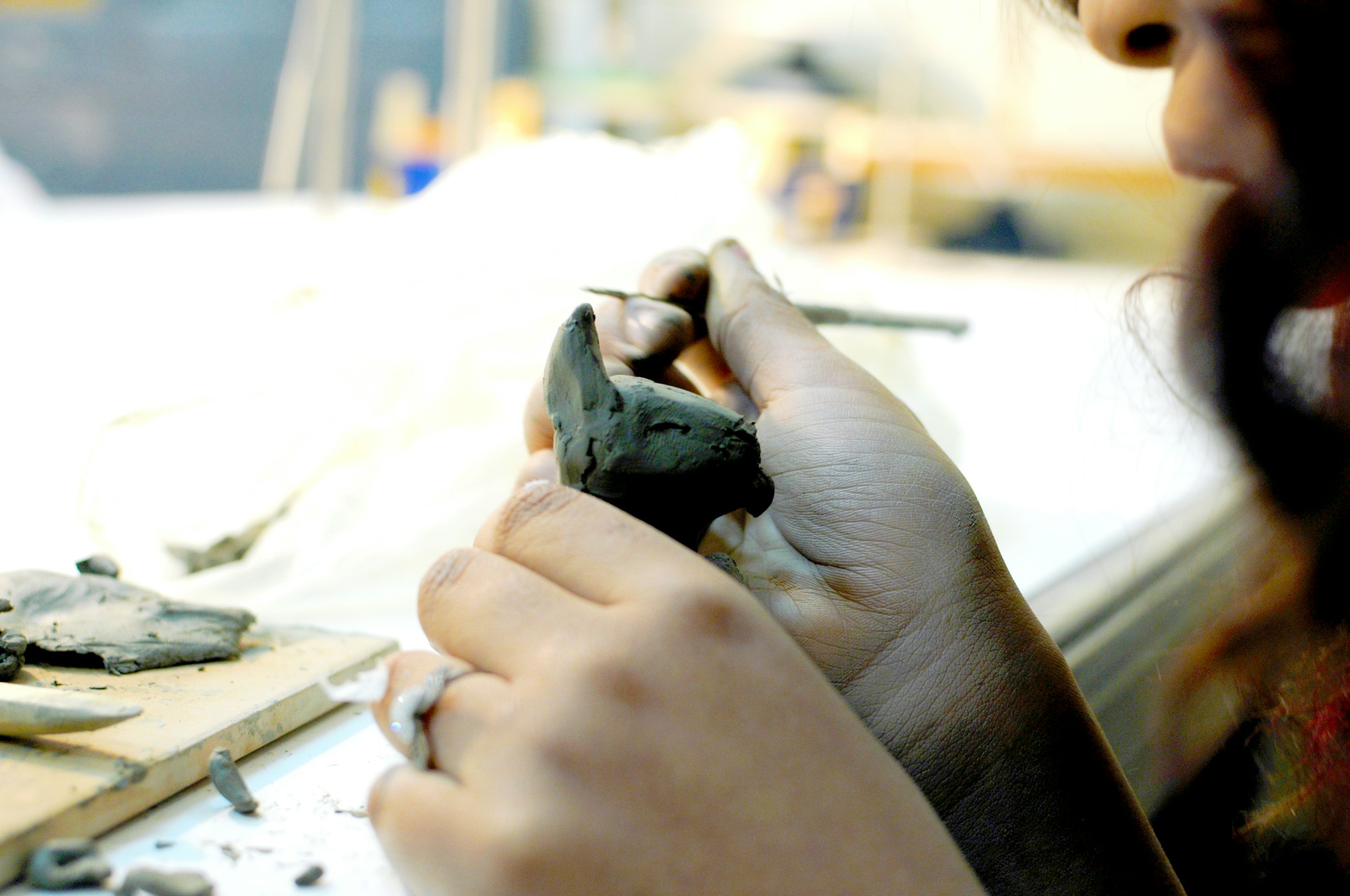 Hands shaping a small clay sculpture with a sculpting tool