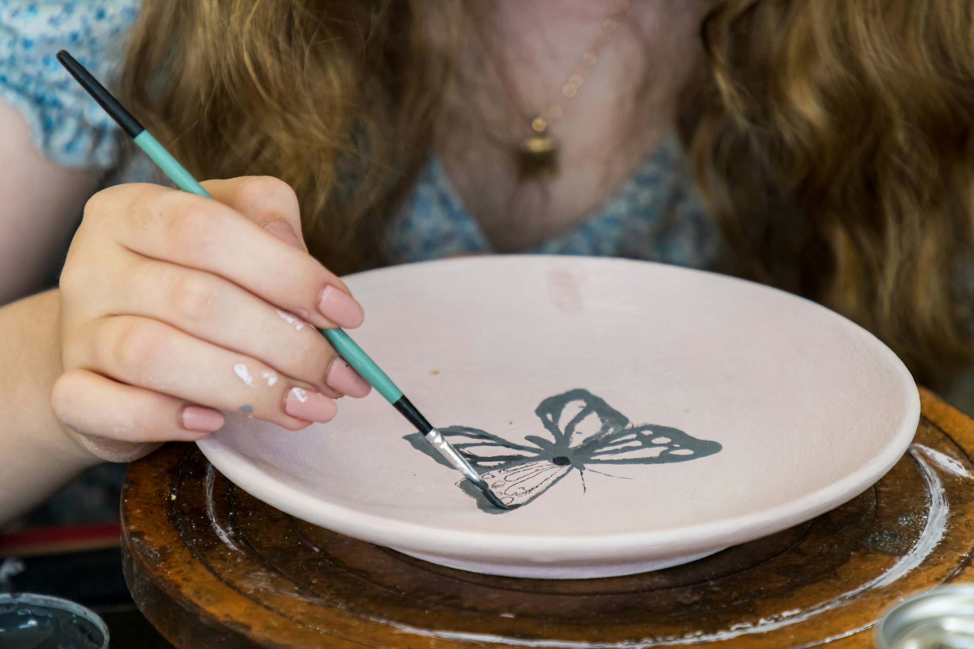 Hands painting a butterfly design onto a ceramic bowl