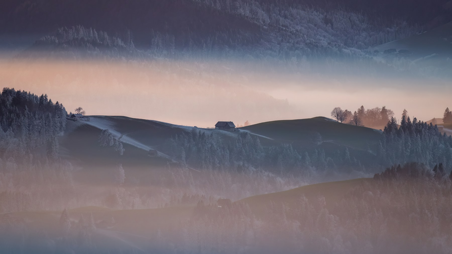 Misty winter hills with a small cabin at sunrise