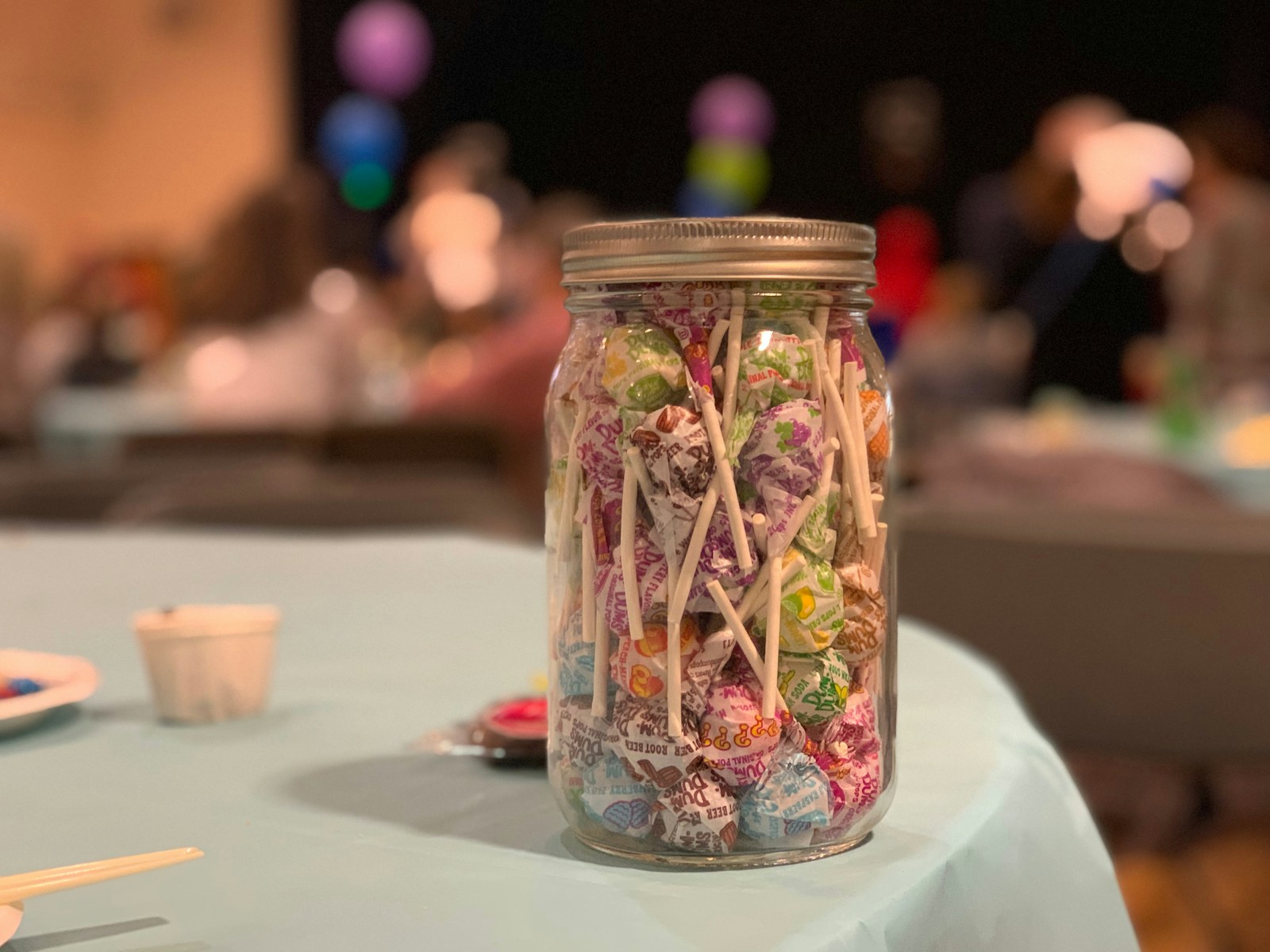 A mason jar packed with colorful lollipops and candies on a party table