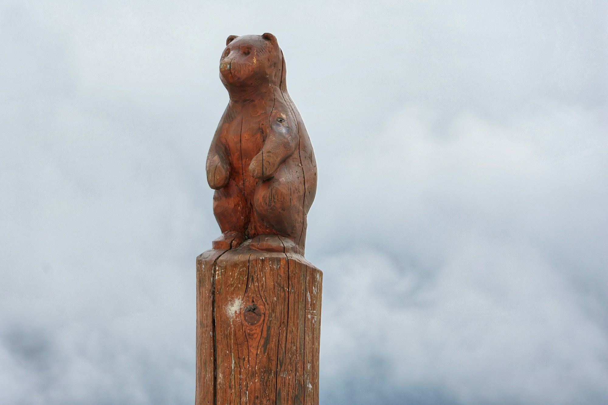 Small carved wooden bear standing on top of a wooden post