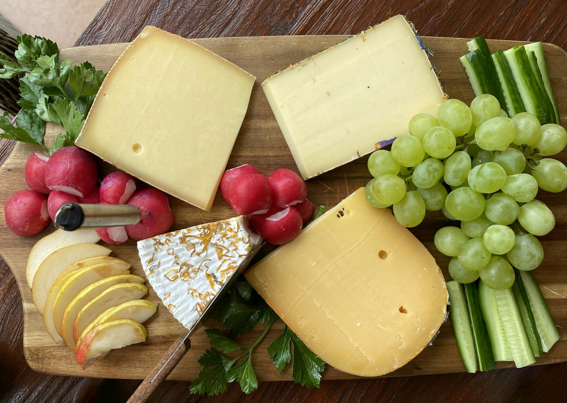 Cutting board Christmas gifts for cheese lovers: a wooden board with cheeses and grapes