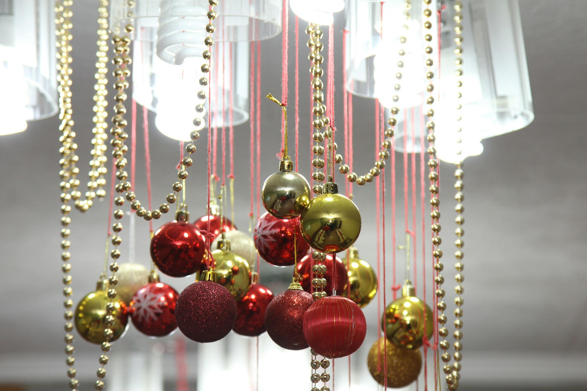 Red and gold ornaments hanging with gold bead strands under a chandelier