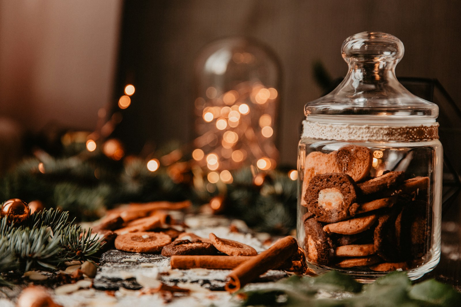 A glass apothecary jar filled with cinnamon cookies beside pine sprigs and fairy lights
