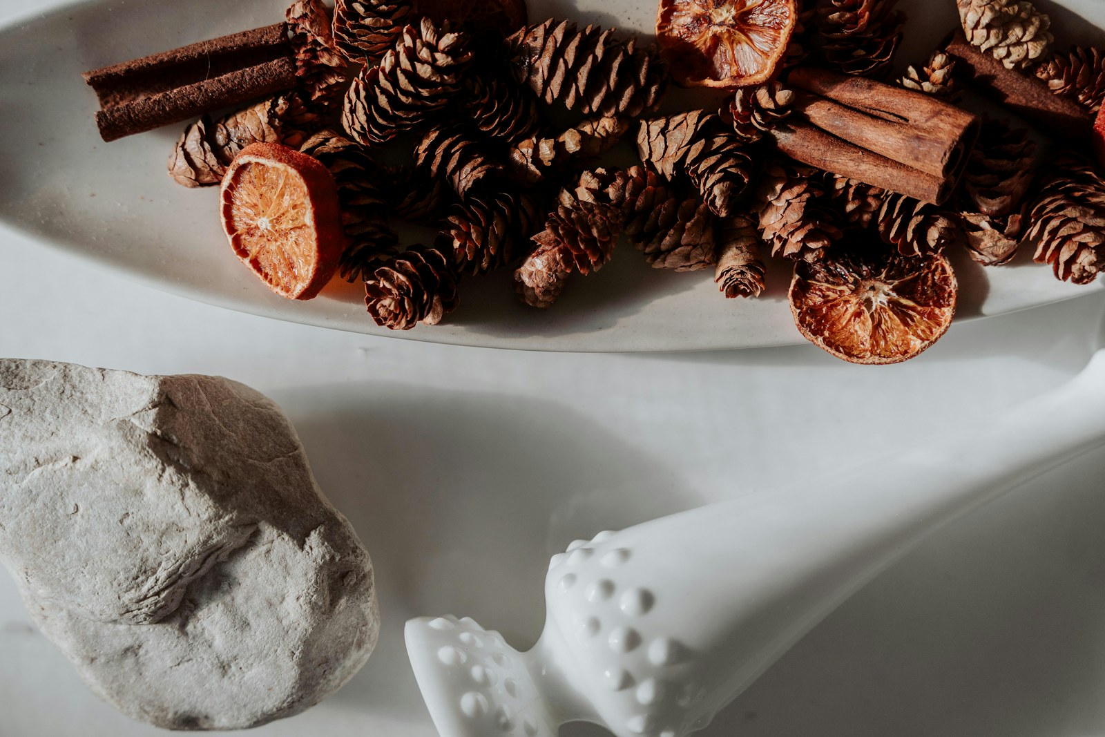 A white bowl filled with pine cones, cinnamon sticks and dried orange slices
