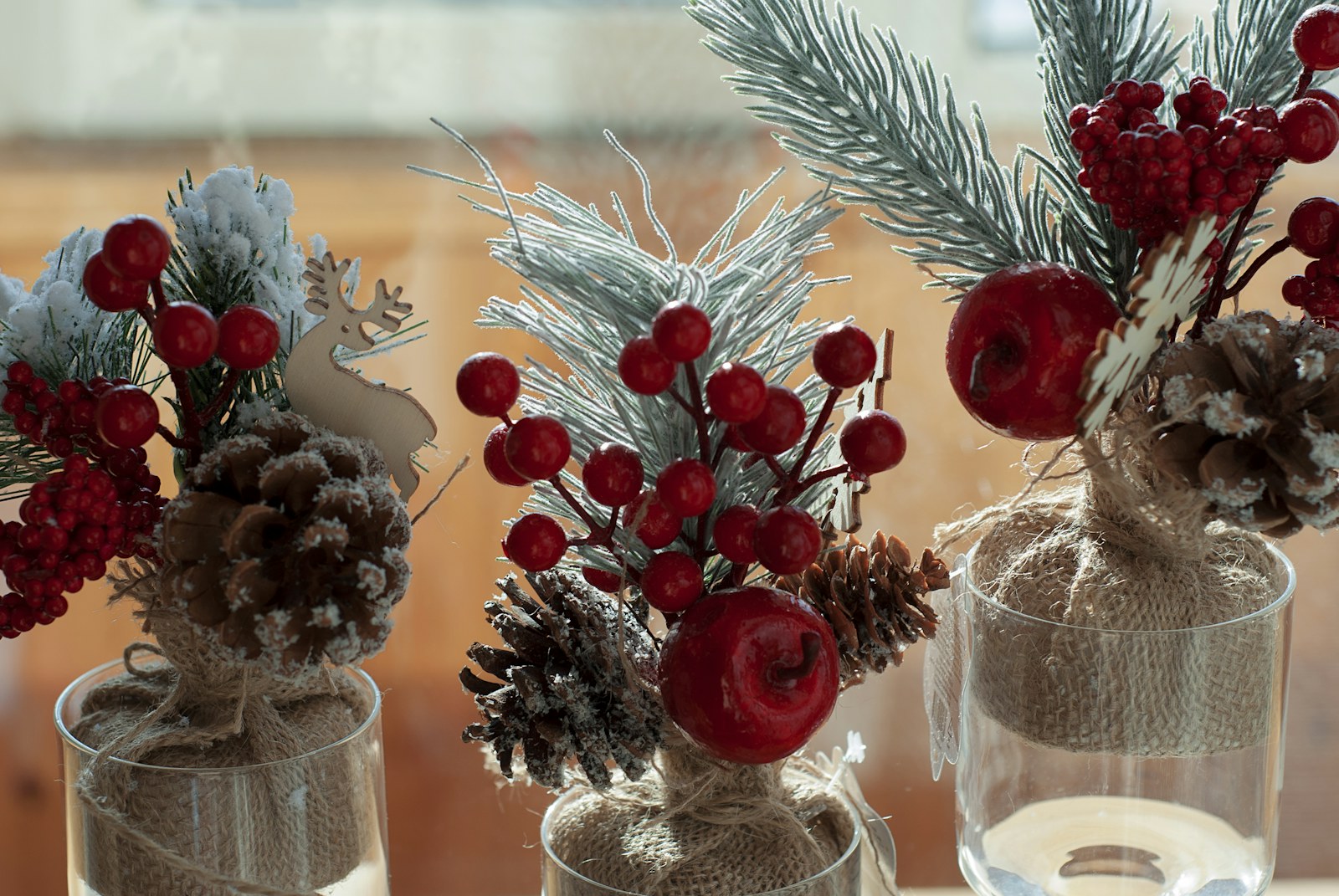 DIY Christmas centerpieces: small jars of pine sprigs, pine cones and red berries on a table