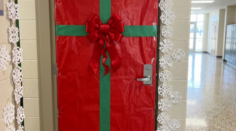 Close up of a Christmas classroom door wrapped in red paper with a green ribbon and a big red bow, paper snowflakes around the frame