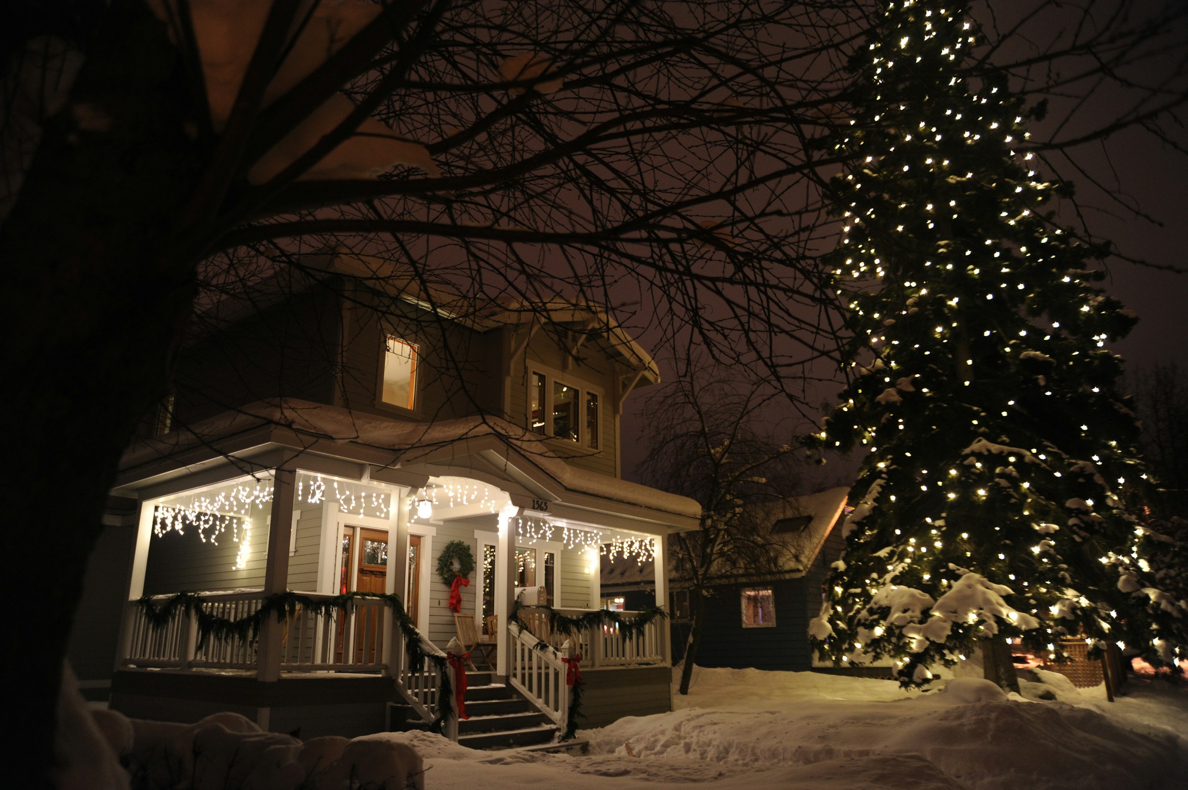 House porch glowing with white twinkle lights and a lit tree in snow
