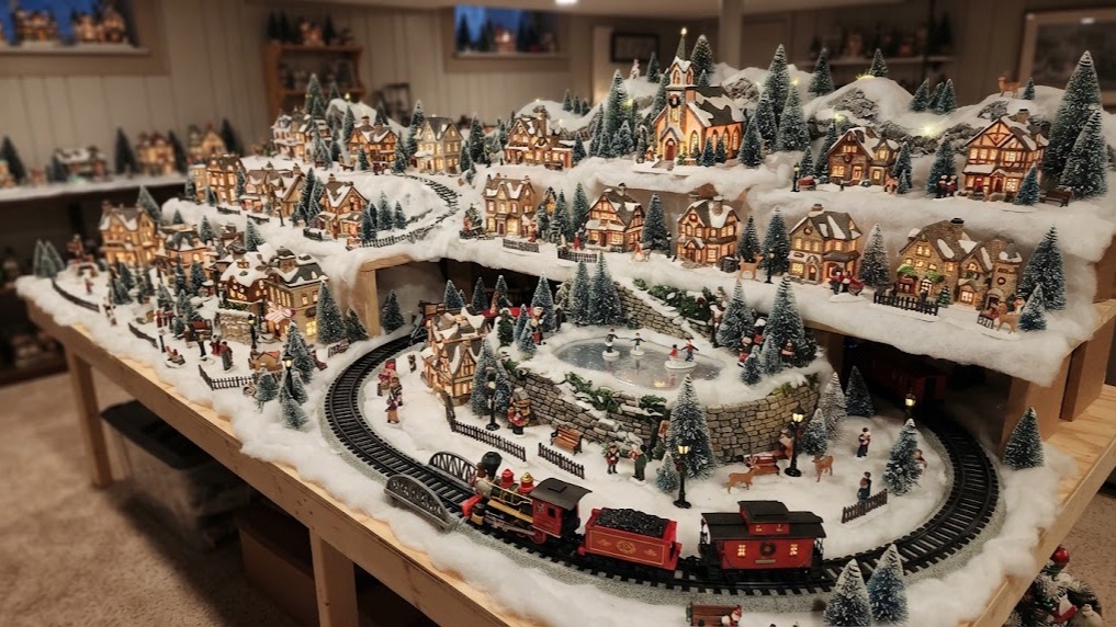 A large homemade Christmas village filling a long table with snowy hills, lit houses and a train