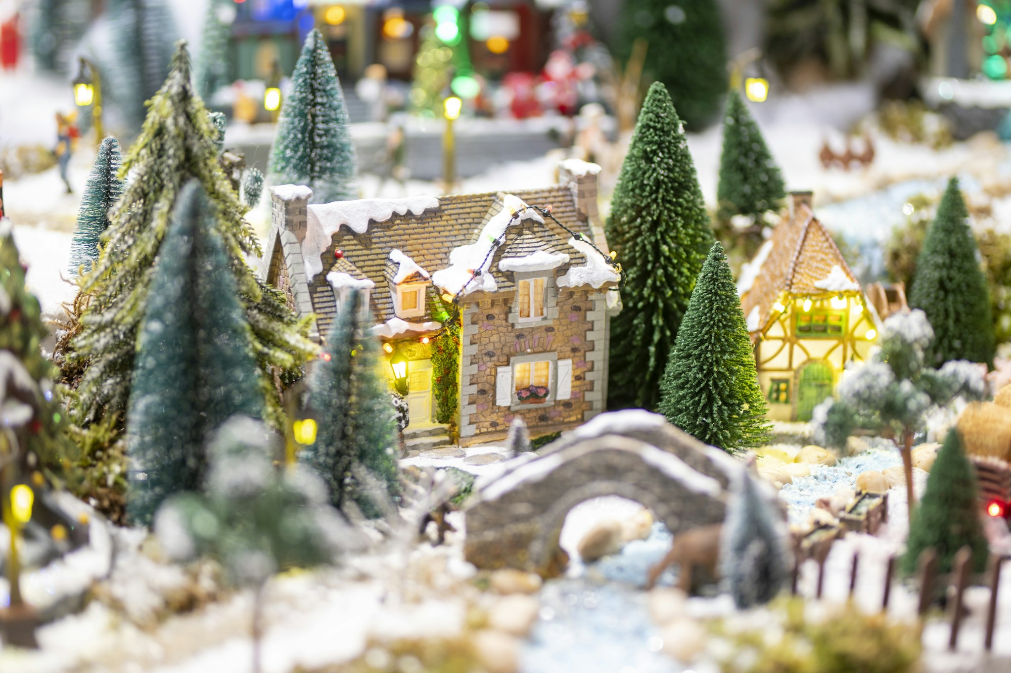 A miniature snowy village with clusters of bottle brush trees and a little stone bridge