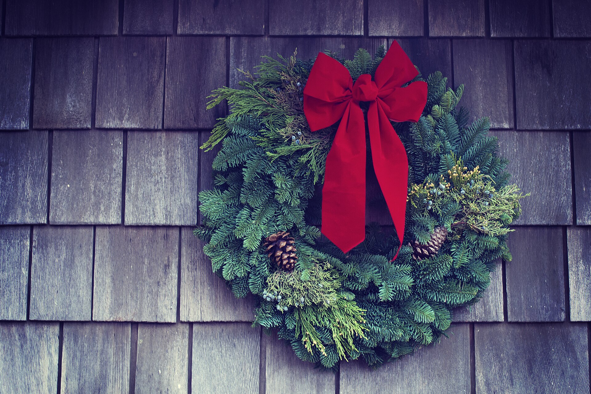 Evergreen Christmas wreath with pinecones and a red bow on a shingle wall