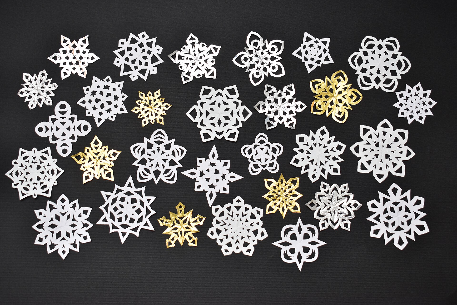 Handmade white and gold paper snowflakes on a dark table
