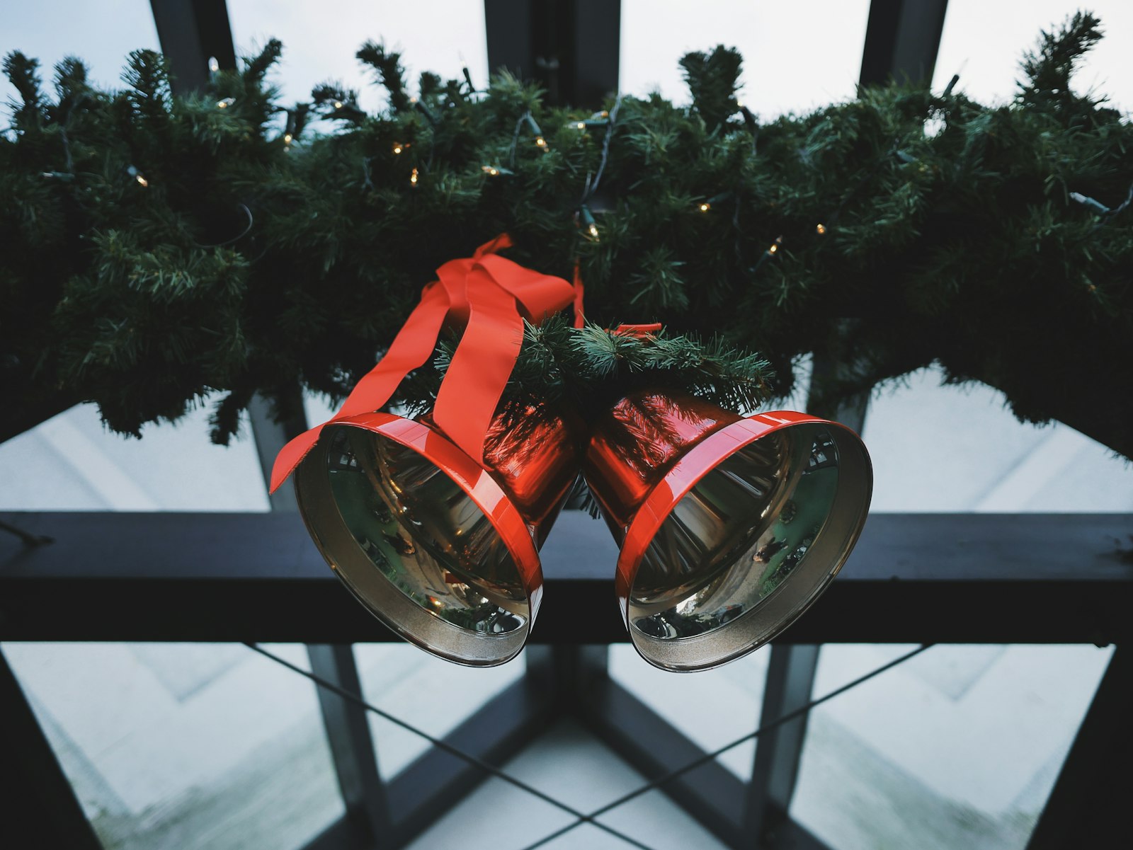 Two red bells tied with ribbon hanging beside evergreen garland