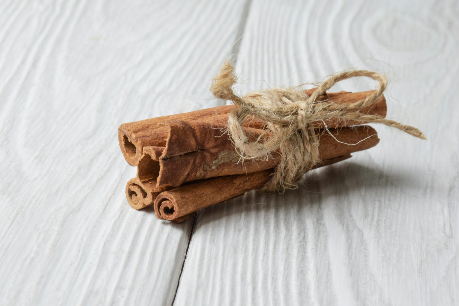 Bundle of cinnamon sticks tied with jute twine on a white wooden table