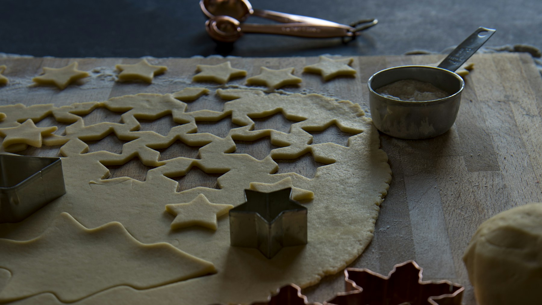 Metal cookie cutters beside rolled dough on a wooden board
