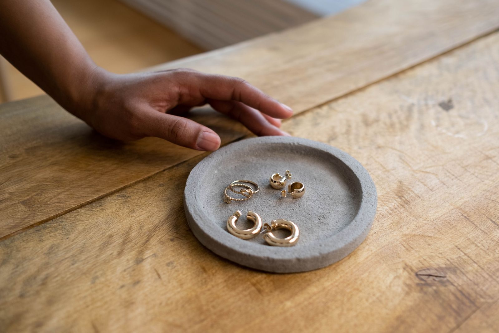 Round gray handmade trinket dish holding gold earrings on a wooden table