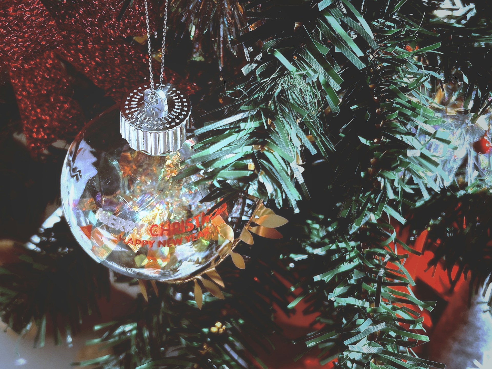 Clear ornament filled with colorful confetti and shiny tinsel hanging on a Christmas tree